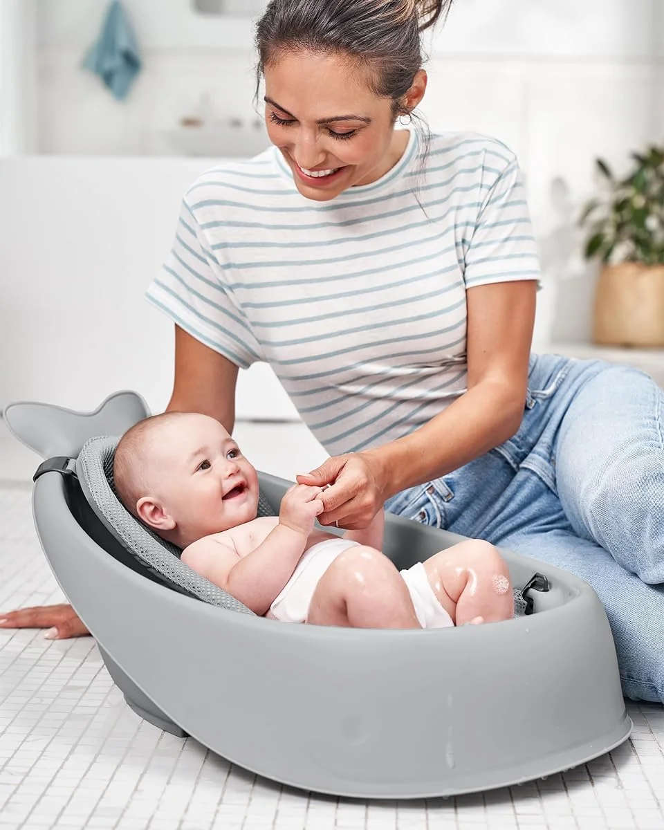 Parent bathing a smiling baby seated in the Skip Hop Moby grey tub during use