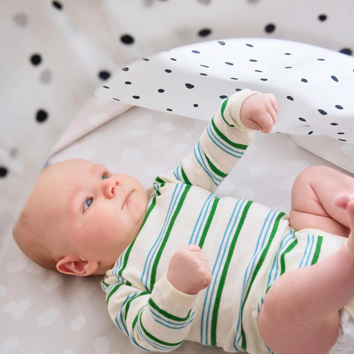 Baby lying under the Lovevery Play Gym arch reaching up for the spotted canopy panel