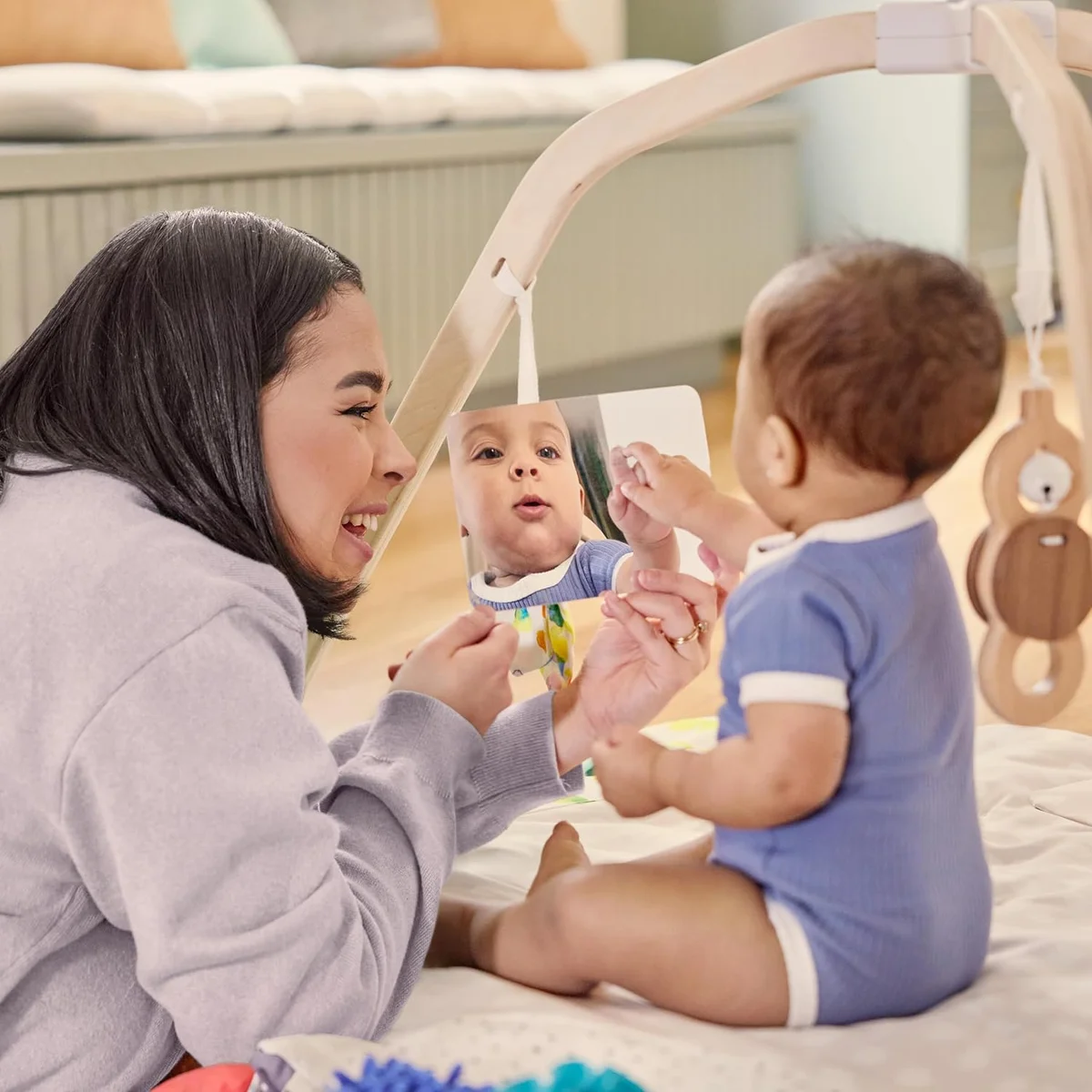 Parent and baby playing with the Lovevery Play Gym peek-a-boo mirror card and wooden batting toy