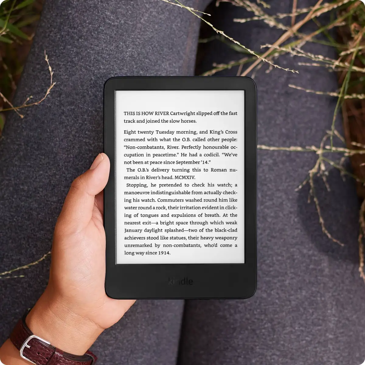 Hand holding the black Amazon Kindle (2024) outdoors over dark fabric