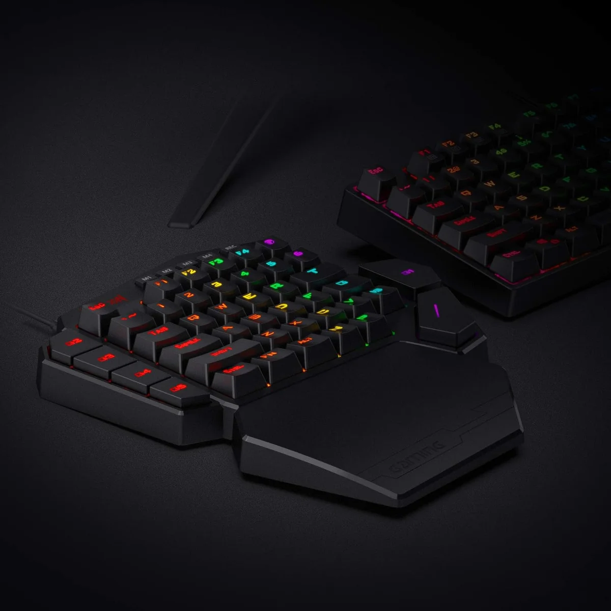 Redragon K585 DITI keypad and detached wrist rest on a desk beside a full-size RGB keyboard, showing scale and setup context