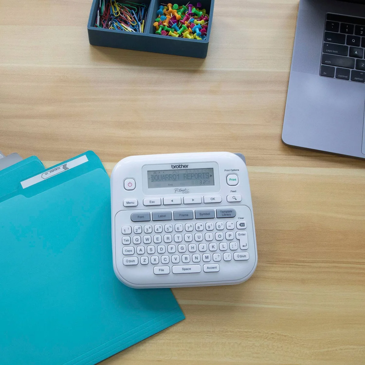 Brother P-Touch PTD220 top-down view on desk with labeled folders and laptop