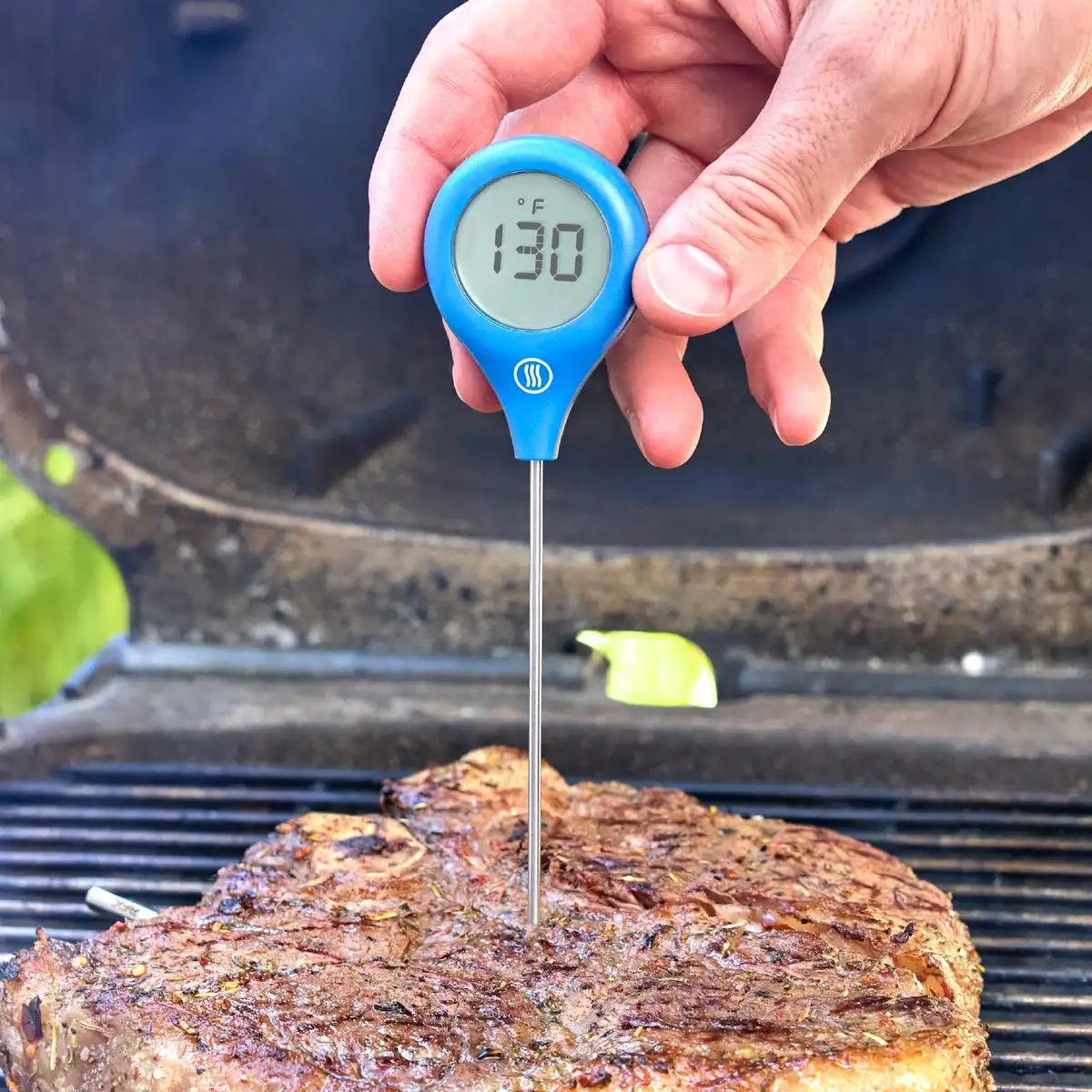 ThermoWorks ThermoPop 2 in blue probing a steak on a grill, display reading 130 degrees F