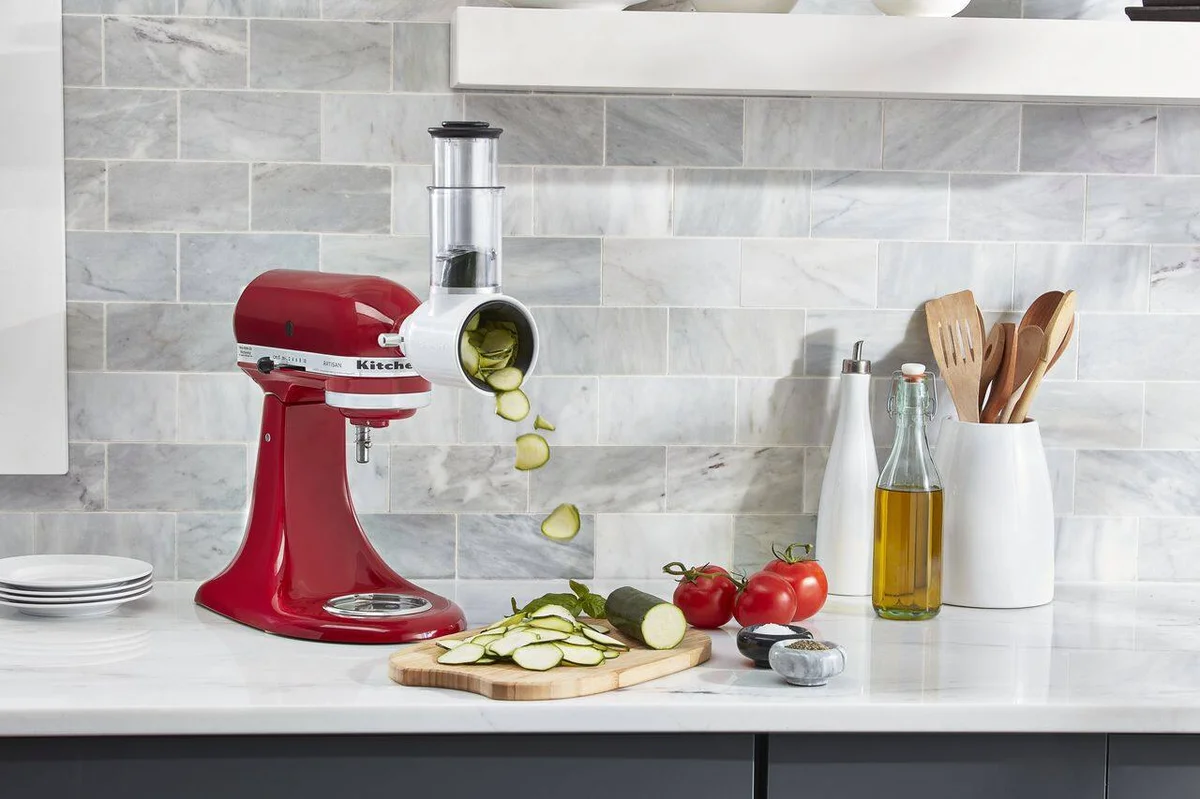KitchenAid Artisan mixer with vegetable slicer attachment slicing zucchini in marble kitchen