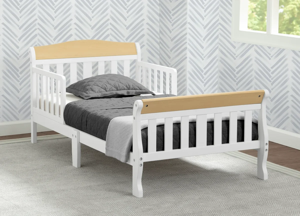 Delta Children Canton Toddler Bed styled in a nursery with grey bedding and patterned wallpaper