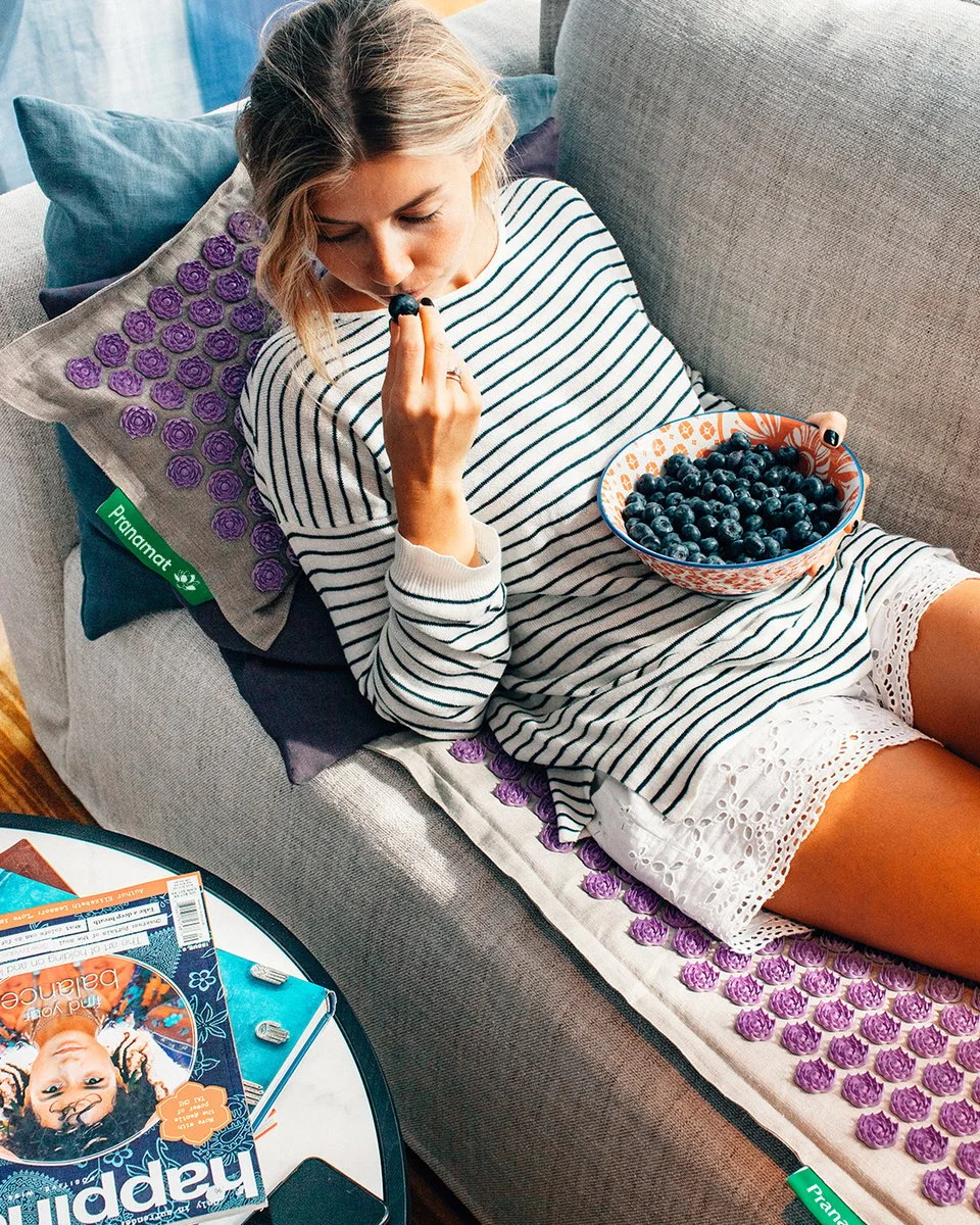 Woman relaxing on the Pranamat ECO acupressure mat and pillow on a sofa
