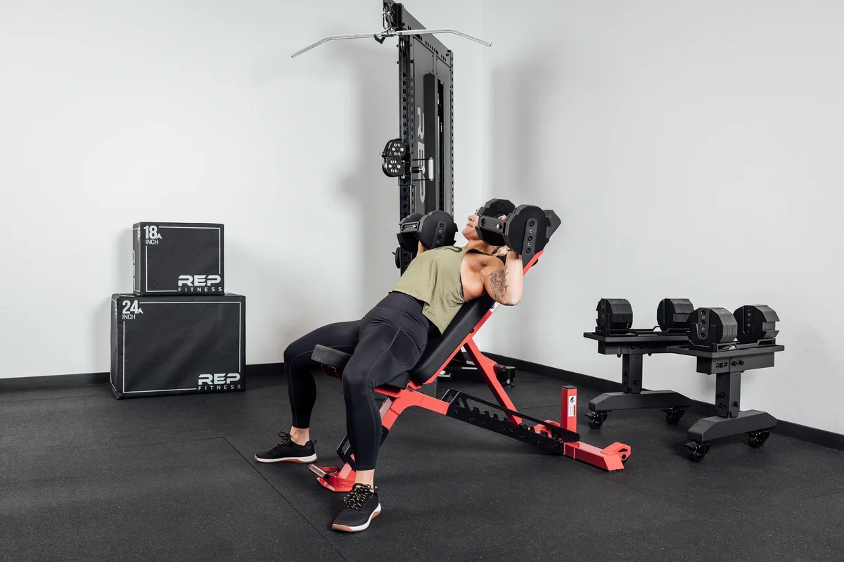 REP Nighthawk Adjustable Bench in use during an incline dumbbell press in a home gym, showing the bench set to an inclined position