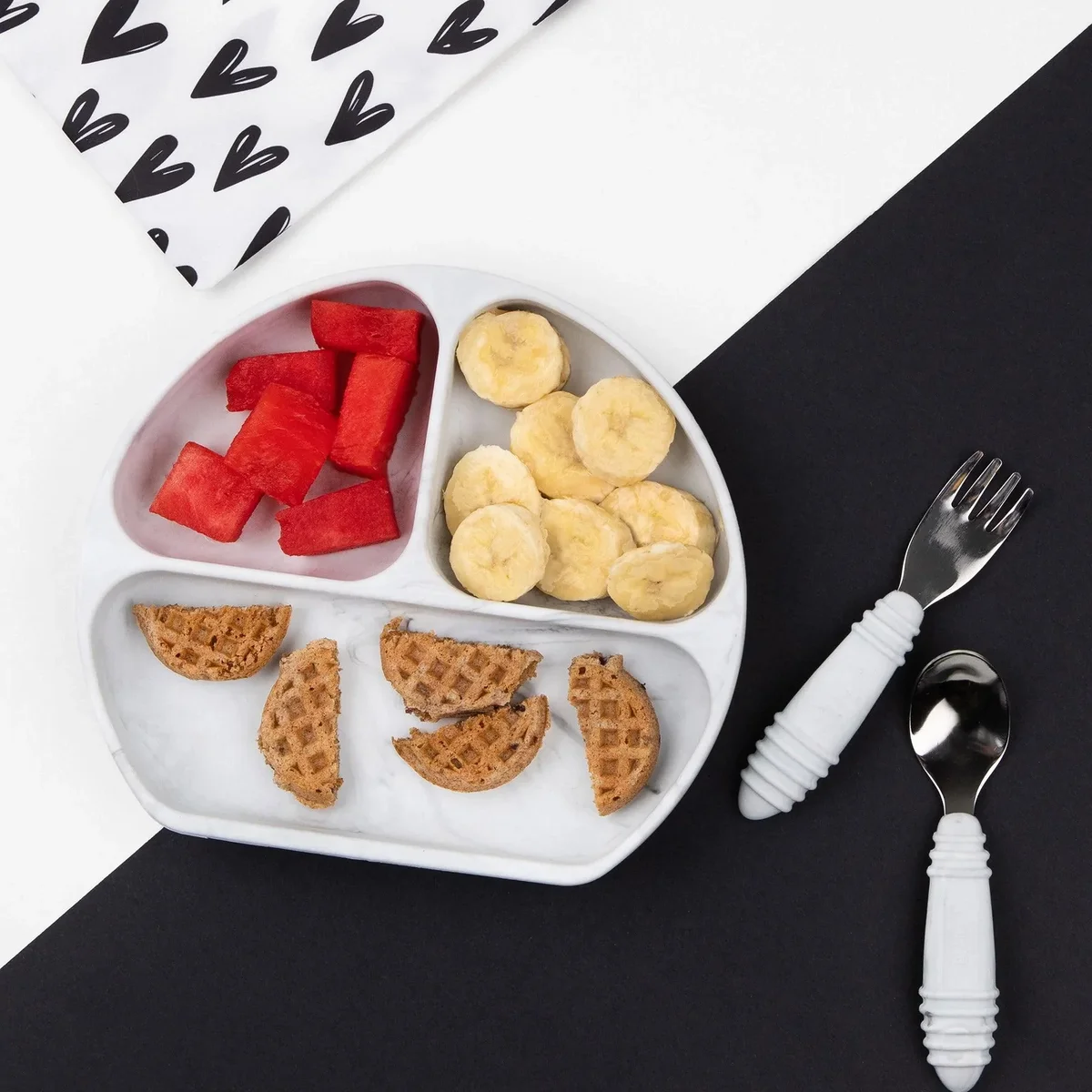 Bumkins Silicone Grip Dish filled with waffles, banana, and watermelon alongside matching utensils