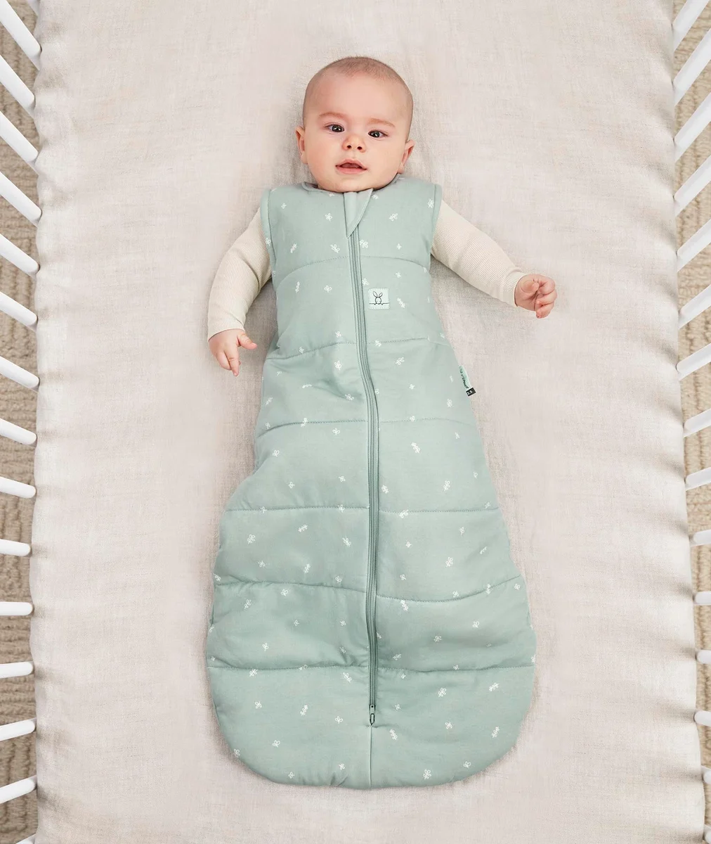 Top-down view of a baby lying in a cot wearing the sage ergoPouch Sleep Sack