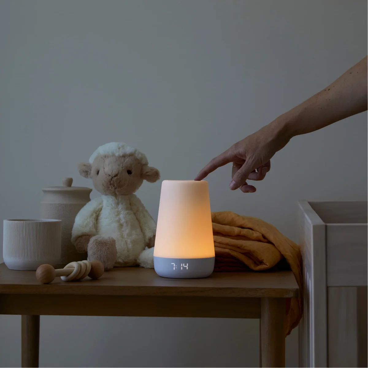 Hatch Rest 2nd Gen glowing warm amber on nursery dresser with hand touching touch ring