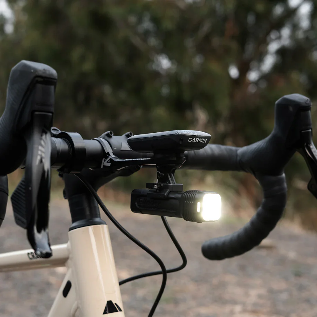 Knog Blinder 1300 mounted on road bike handlebars with beam on, outdoor trail setting
