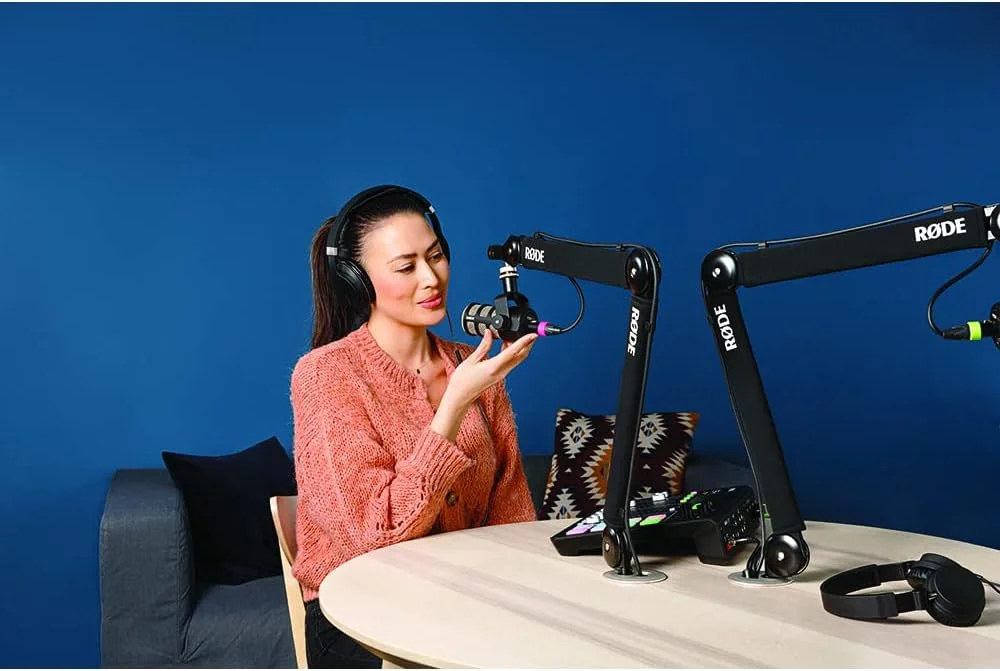 Podcaster using the RØDE PSA1+ boom arm with a microphone at a desk, showing real-world studio setup