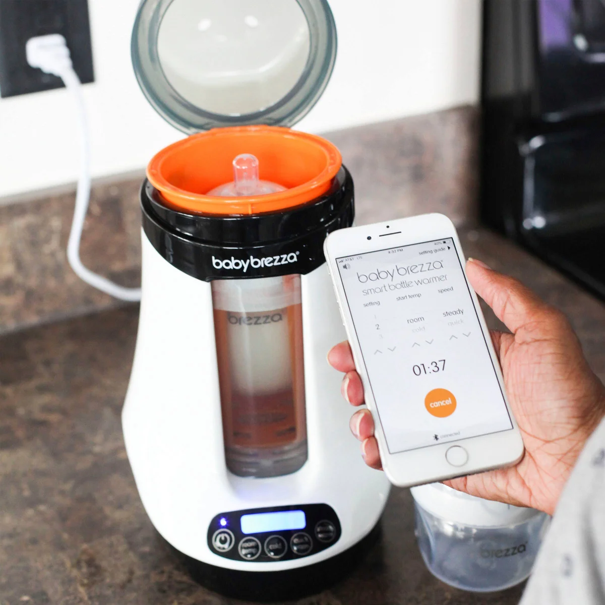 Baby Brezza Safe & Smart Bottle Warmer in use on kitchen counter with Bluetooth app on smartphone