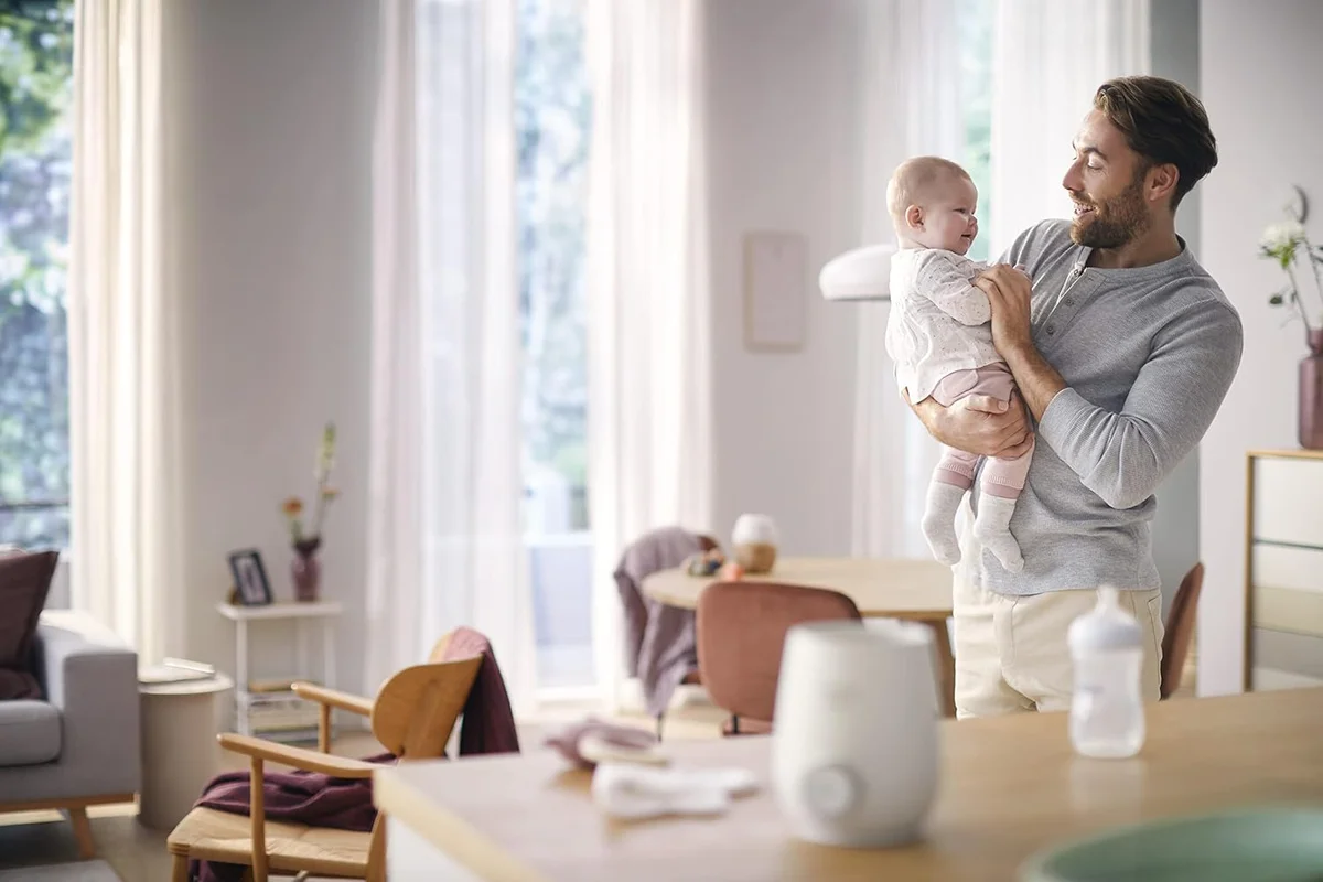 Philips Avent Premium Fast Bottle Warmer in use on kitchen table, father and baby in background