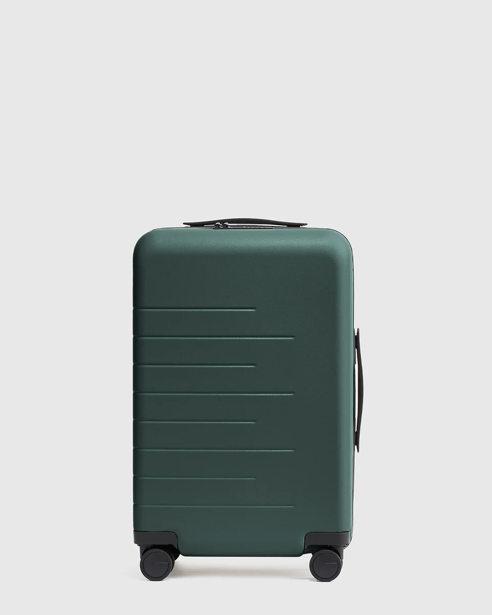 Quince Carry-On Hard Shell Suitcase front view in dark green showing polycarbonate shell and spinner wheels
