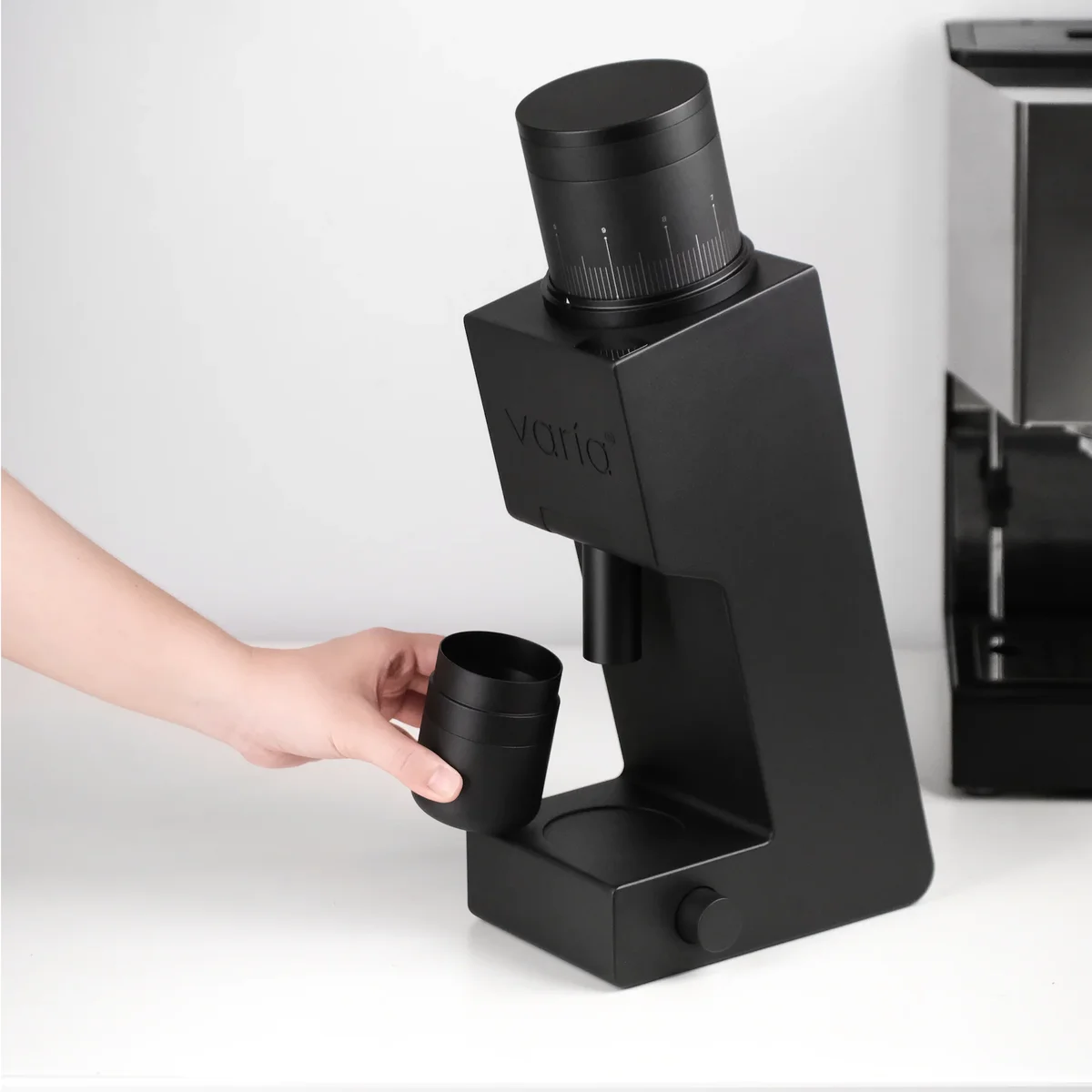 Hand removing the grounds cup from the Varia VS6 grinder, showing the output chute from a side angle