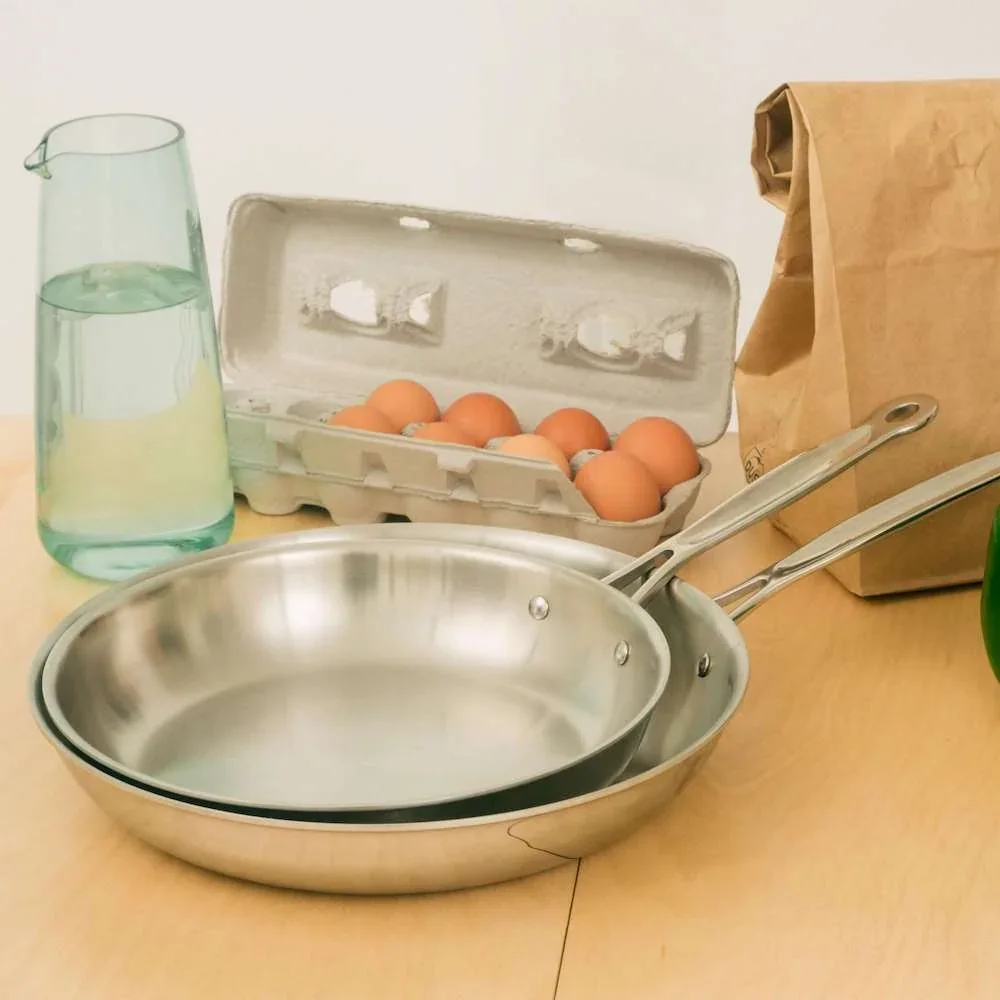 Goldilocks 8-Piece Cookware Set fry pans in use on a kitchen table with eggs and water pitcher