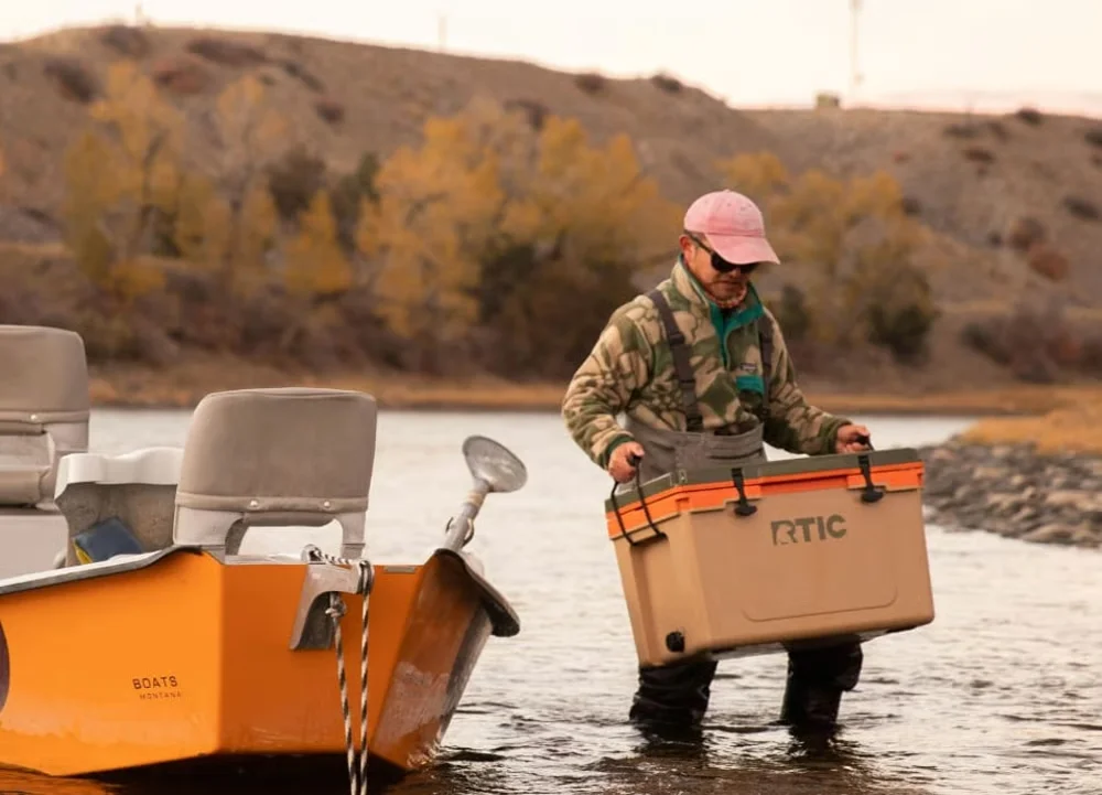 RTIC Ultra-Light 52Q being carried into a boat at a river — lifestyle in-use shot