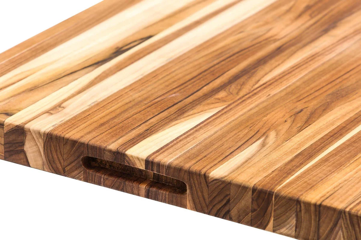 Close-up of the Teakhaus Extra-Large Professional Cutting Board's corner, showing the edge-grain teak wood grain and the carved hand grip slot