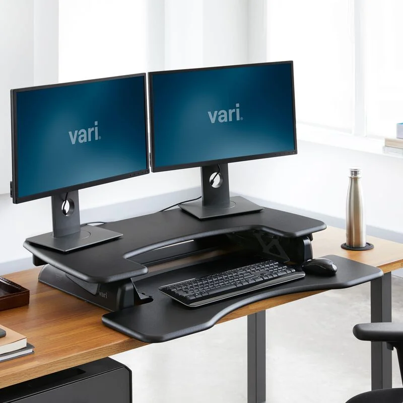 VariDesk Pro Plus 36 in lowered sitting position with dual monitors on a warm wood desk