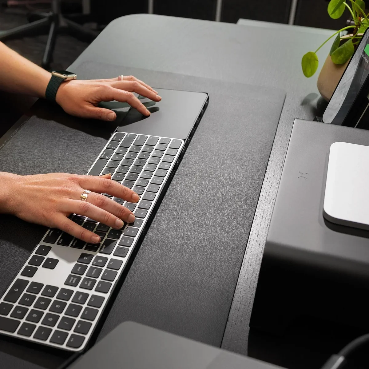 Hands typing on a Magic Keyboard atop the black Twelve South DeskPad on a desk, in-use lifestyle