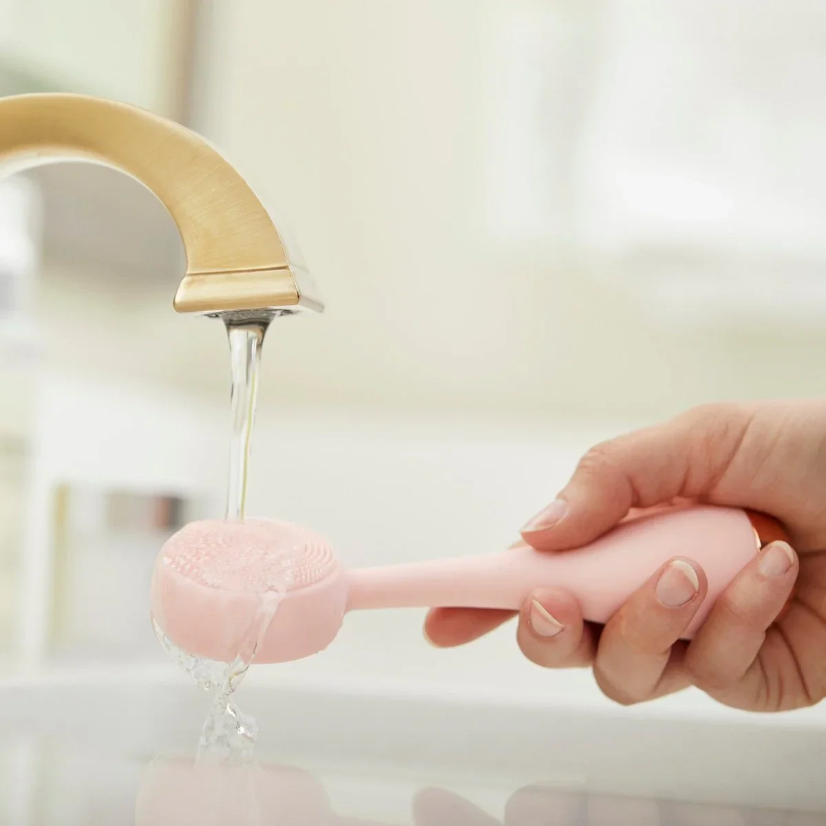 PMD Clean silicone brush head being rinsed under running water at a faucet