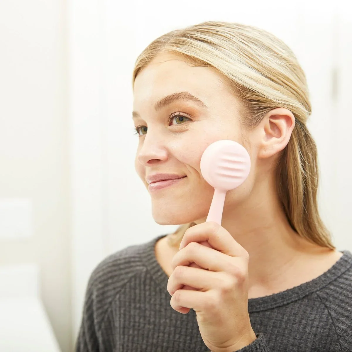 PMD Clean held by a woman showing the smooth massager side against her cheek