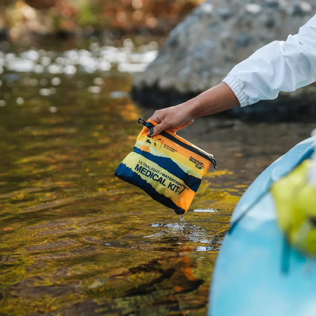 Adventure Medical Kits Ultralight/Watertight .7 kit held over a river demonstrating its waterproof design