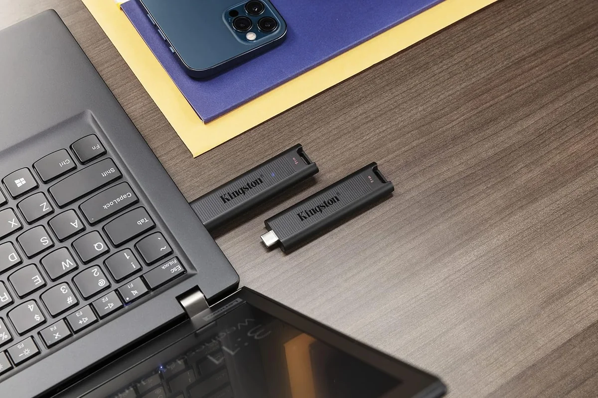 Two Kingston DataTraveler Max USB-C flash drives on a desk next to a laptop and phone