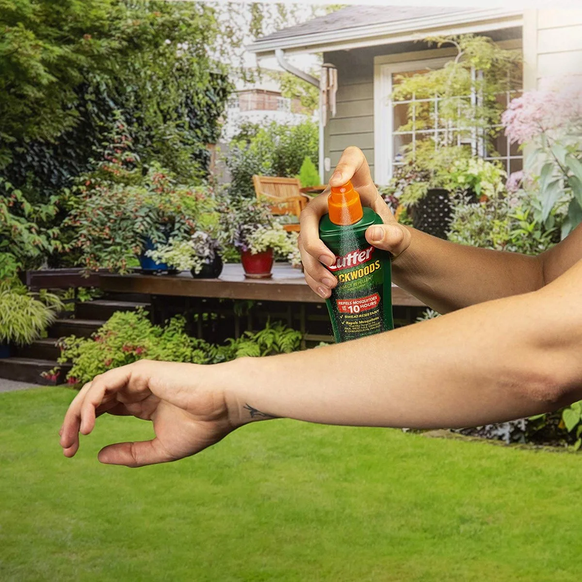 Person applying Cutter Backwoods insect repellent to arm while outdoors in a garden