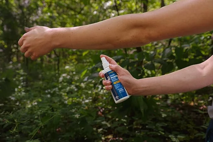 Person spraying Sawyer Picaridin insect repellent on arm in forest setting