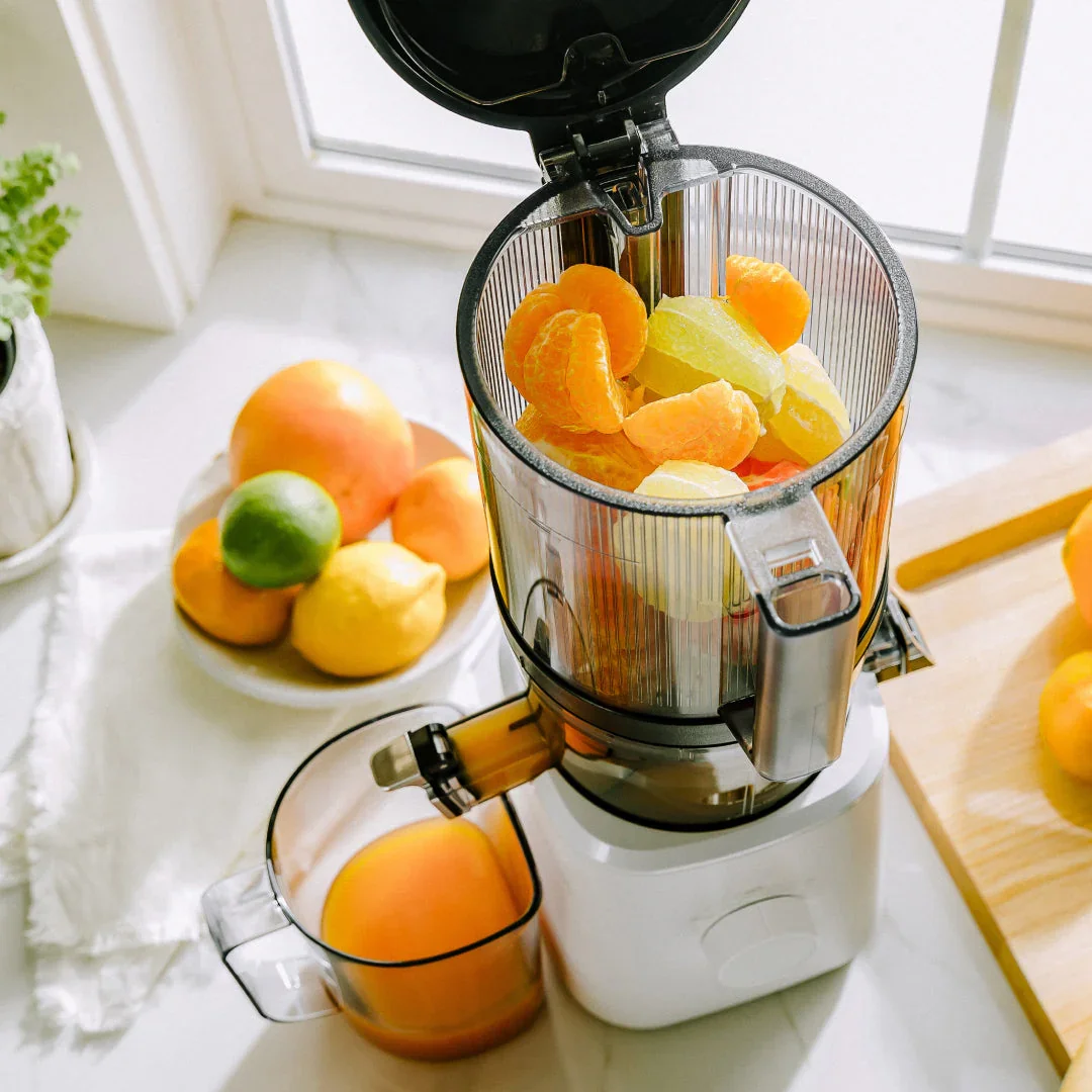 Nama J2 Cold Press Juicer hopper loaded with citrus fruit, fresh orange juice collecting in cup below