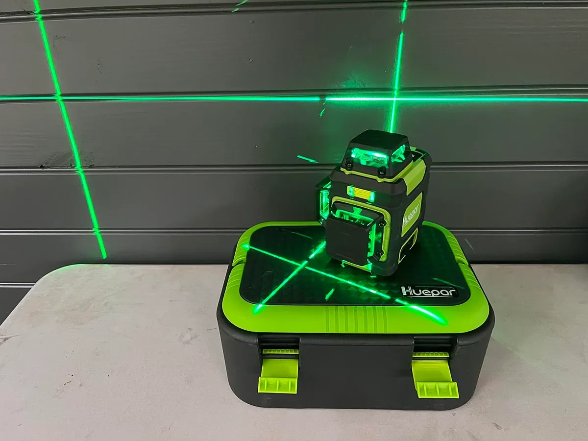 Huepar HM03CG projecting three green 360-degree laser planes onto a dark wall panel