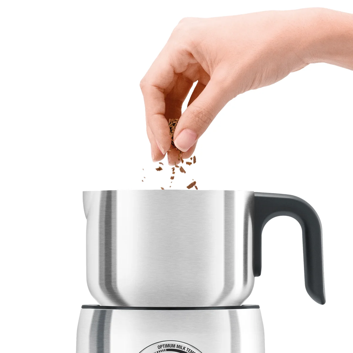 Close-up of a hand sprinkling chocolate shavings into the Breville Milk Café's stainless steel pitcher