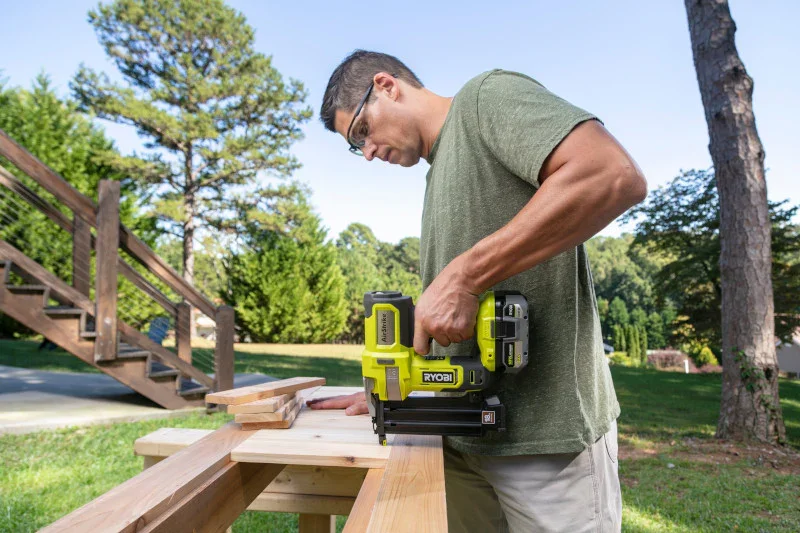 Ryobi AirStrike brad nailer in use outdoors, person nailing a wood plank on a sawhorse