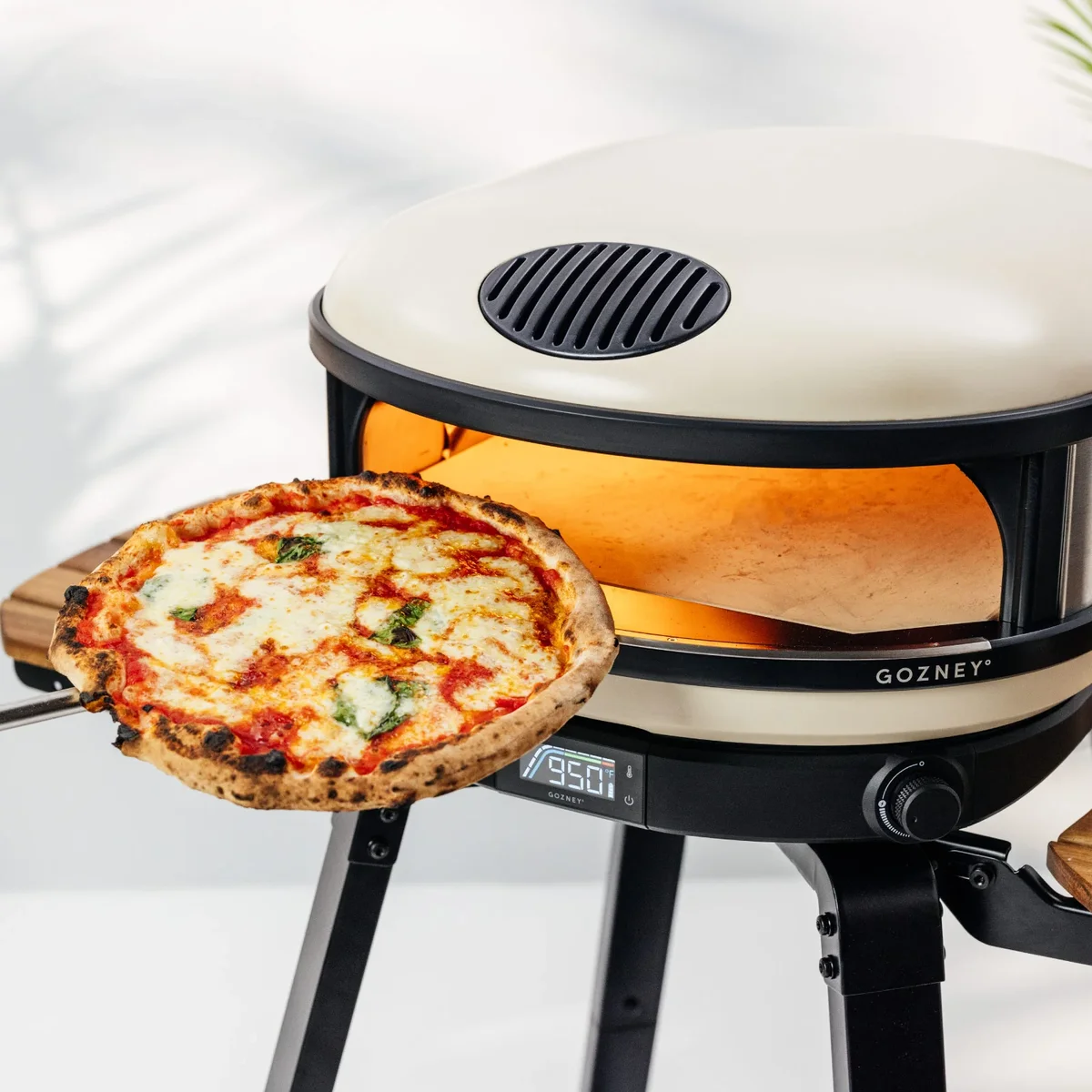 Gozney Arc XL pizza oven on patio with a charred Margherita pizza being pulled out on a wooden peel