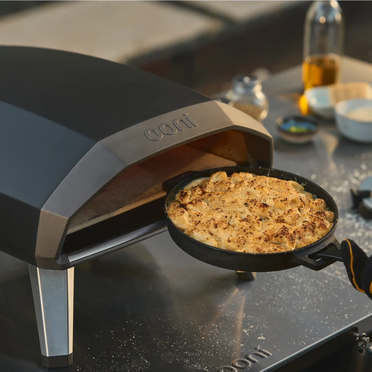 Close-up of the Ooni Koda 2 door and Ooni badge as a cast iron skillet of baked mac and cheese is pulled from the oven