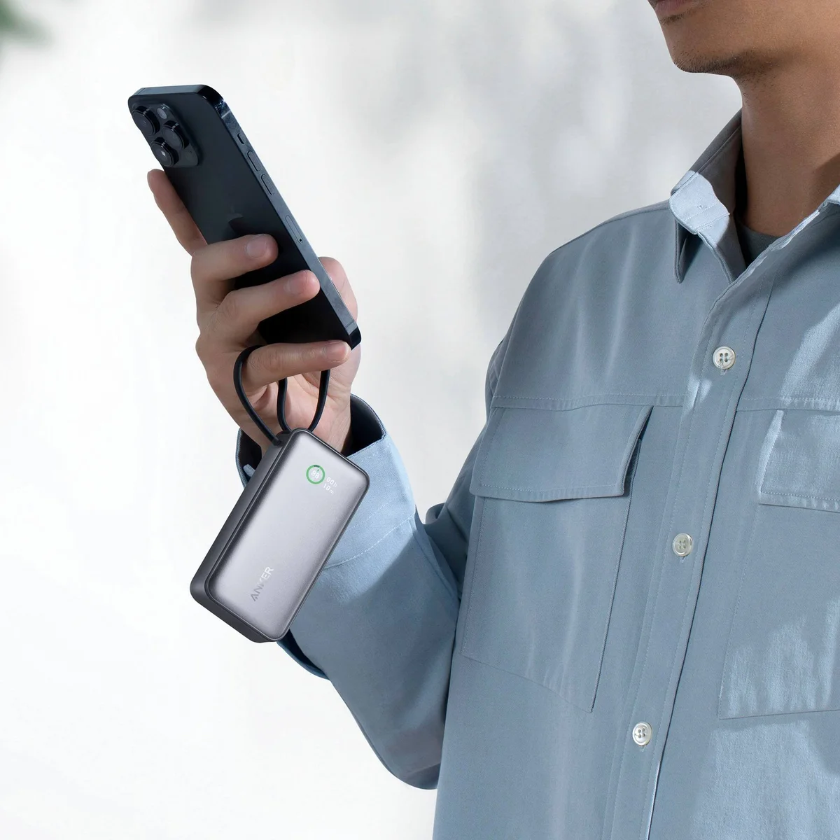 Anker Nano Power Bank 10K 30W hanging from its built-in cable strap while a person holds a phone