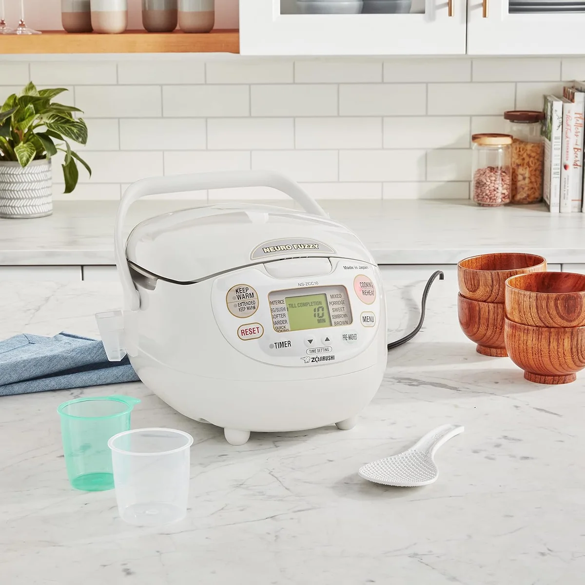 Zojirushi NS-ZCC10 rice cooker on a kitchen counter with rice paddle, measuring cups, and wooden bowls
