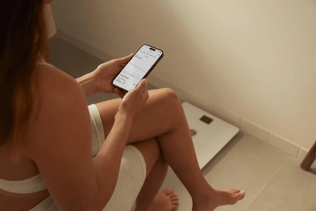 Person reviewing Withings Health Mate app in bathroom with Body Smart scale in background