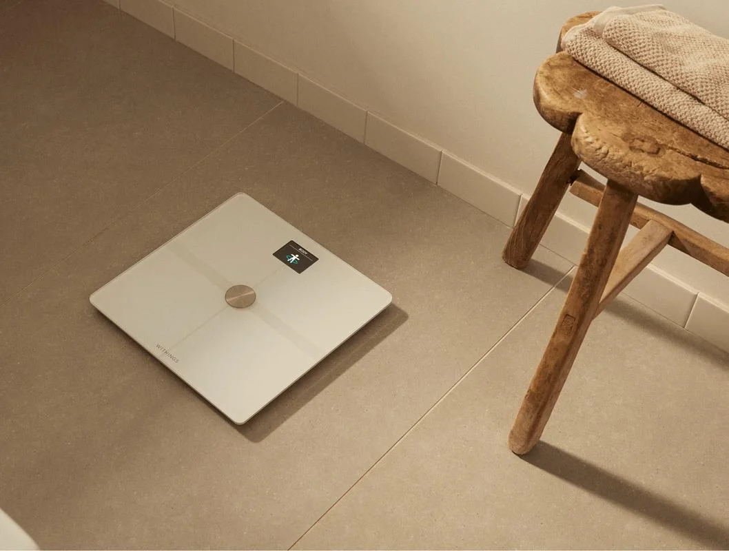 Withings Body Smart scale on bathroom tile floor next to rustic wooden stool