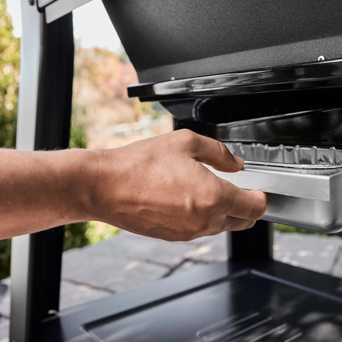 Close-up of a hand sliding out the Weber Searwood XL's stainless steel grease and ash tray for cleanup