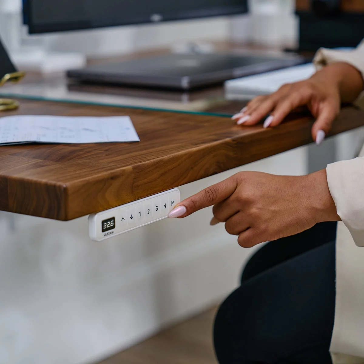 Close-up of the UPLIFT V3 Standing Desk keypad with height display and memory preset buttons, mounted under a walnut desktop