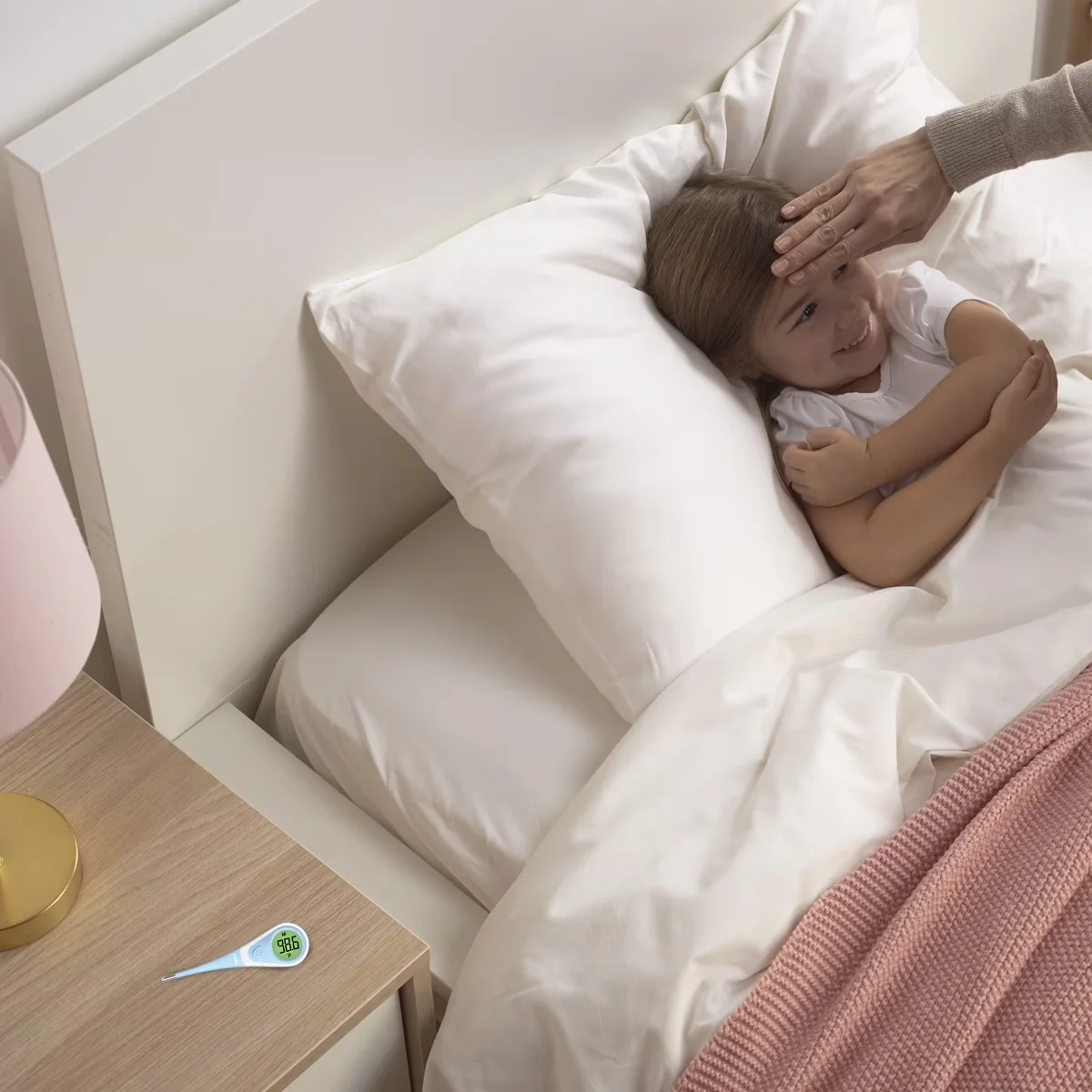 Vicks ComfortFlex thermometer resting on a bedside table next to a child sick in bed