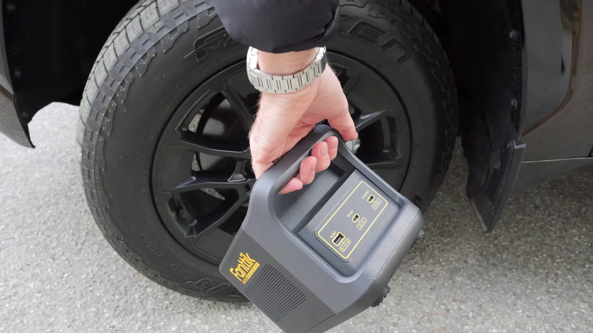 Fanttik X9 Ultra being carried by handle next to a truck tire
